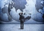 Businessman Stands And Looks Up At Three Interlocking Globes On Wall