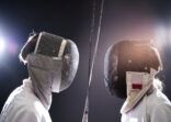 Boys with foils fencing against black background