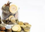 jar of money, various currency coins overflowing on white background